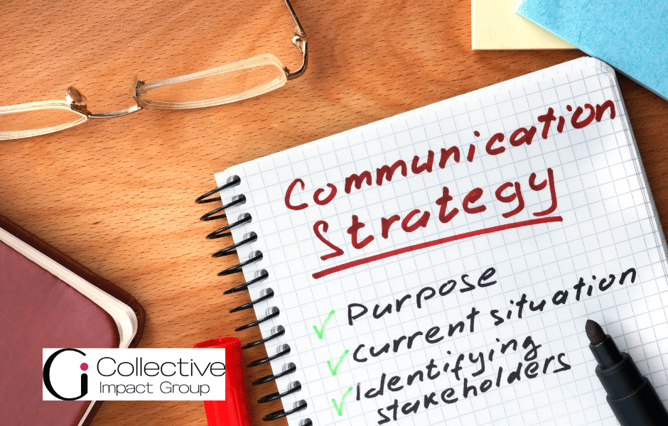 Notebook with the words "Communication Strategy" in red sitting on a table next to a pen and reading glasses